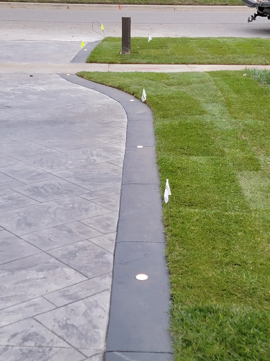 Recessed curb lights set into a driveway edge next to newly laid sod