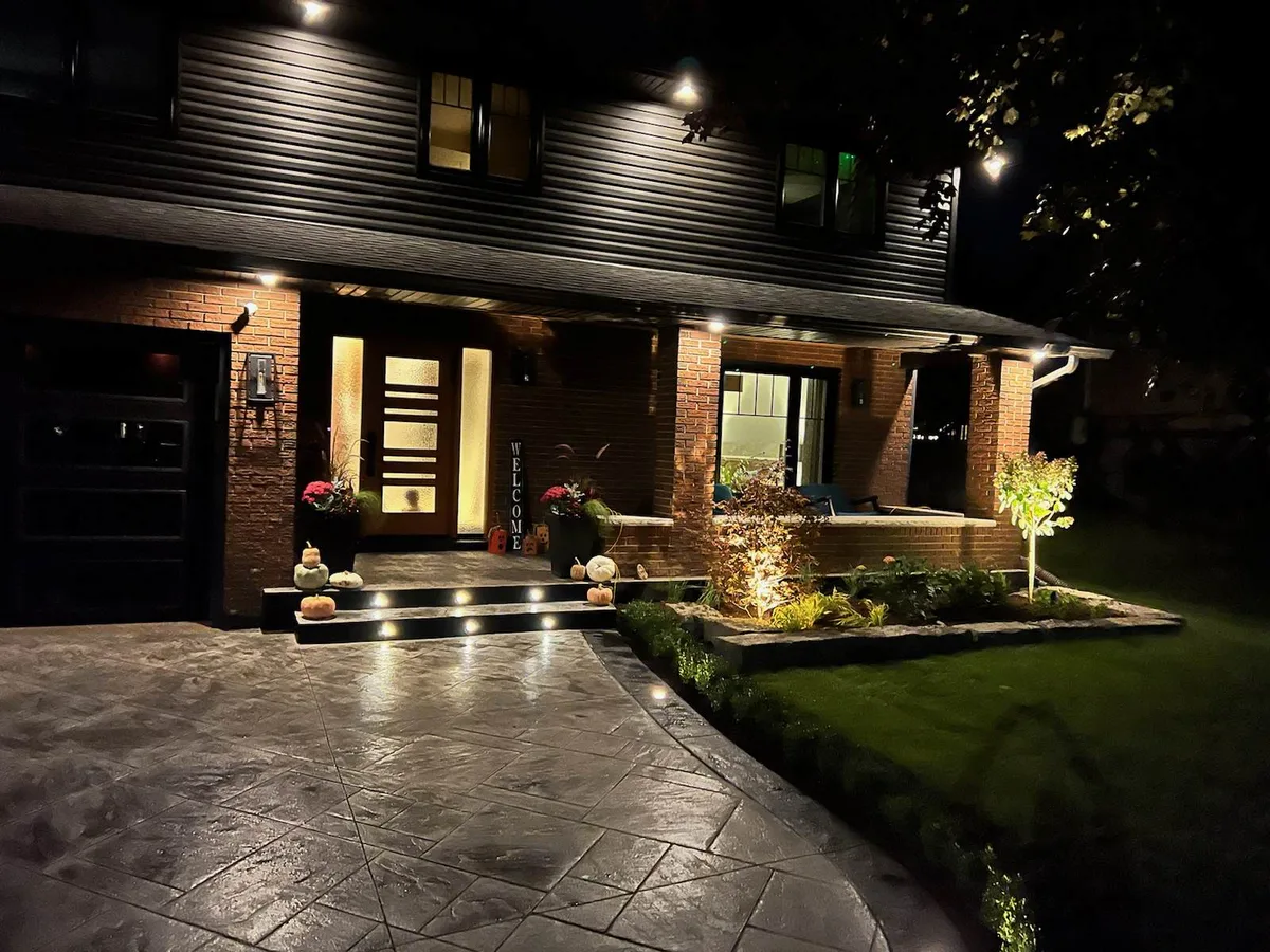 Lit front entrance and driveway at night with uplighting on the garden bed