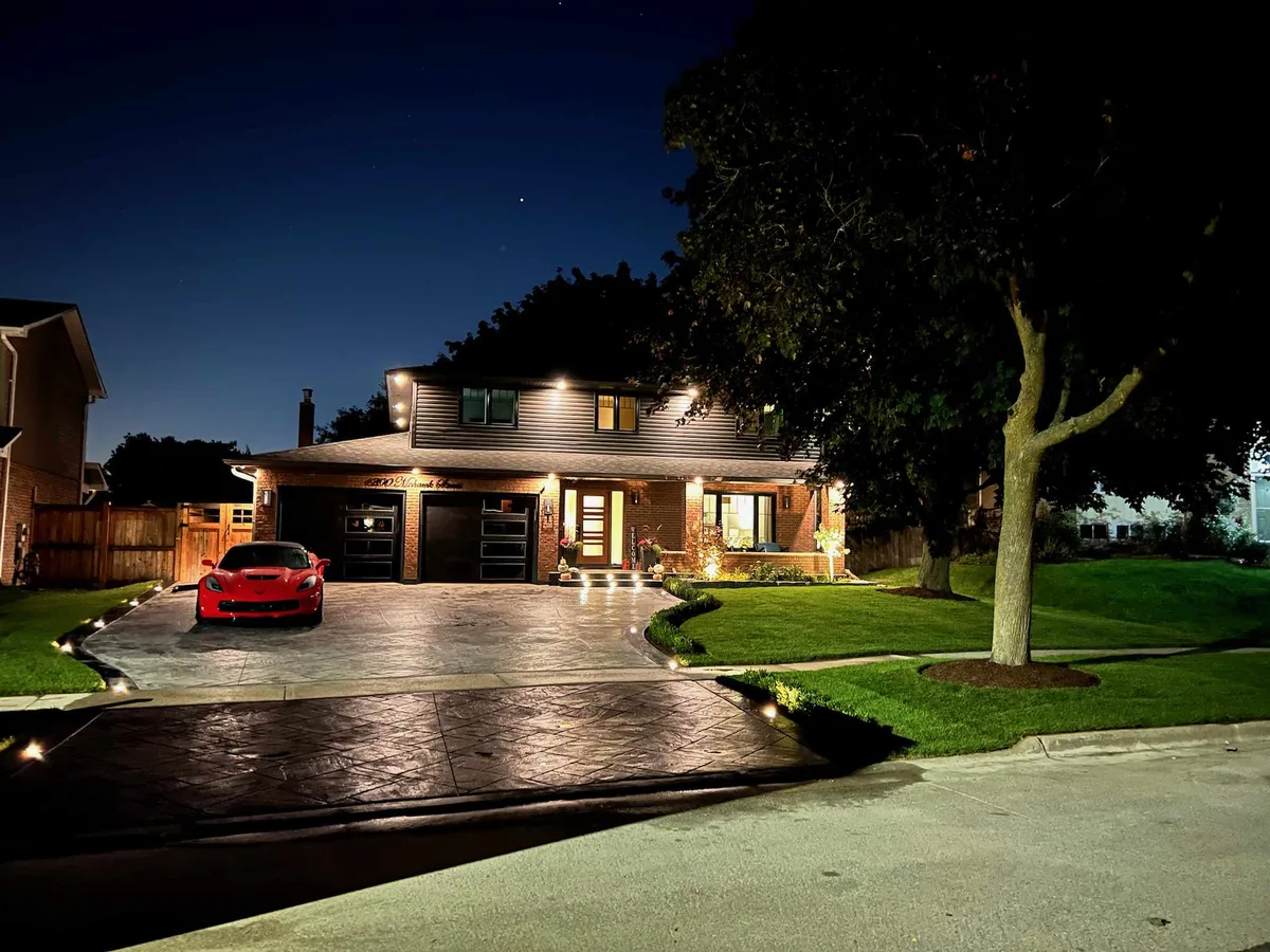 Front yard at night with driveway lights, soffit lighting and a lit lawn