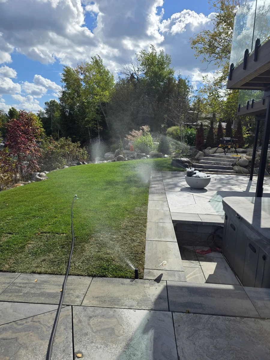 Several irrigation zones running at once across a large sod lawn beside a flagstone patio