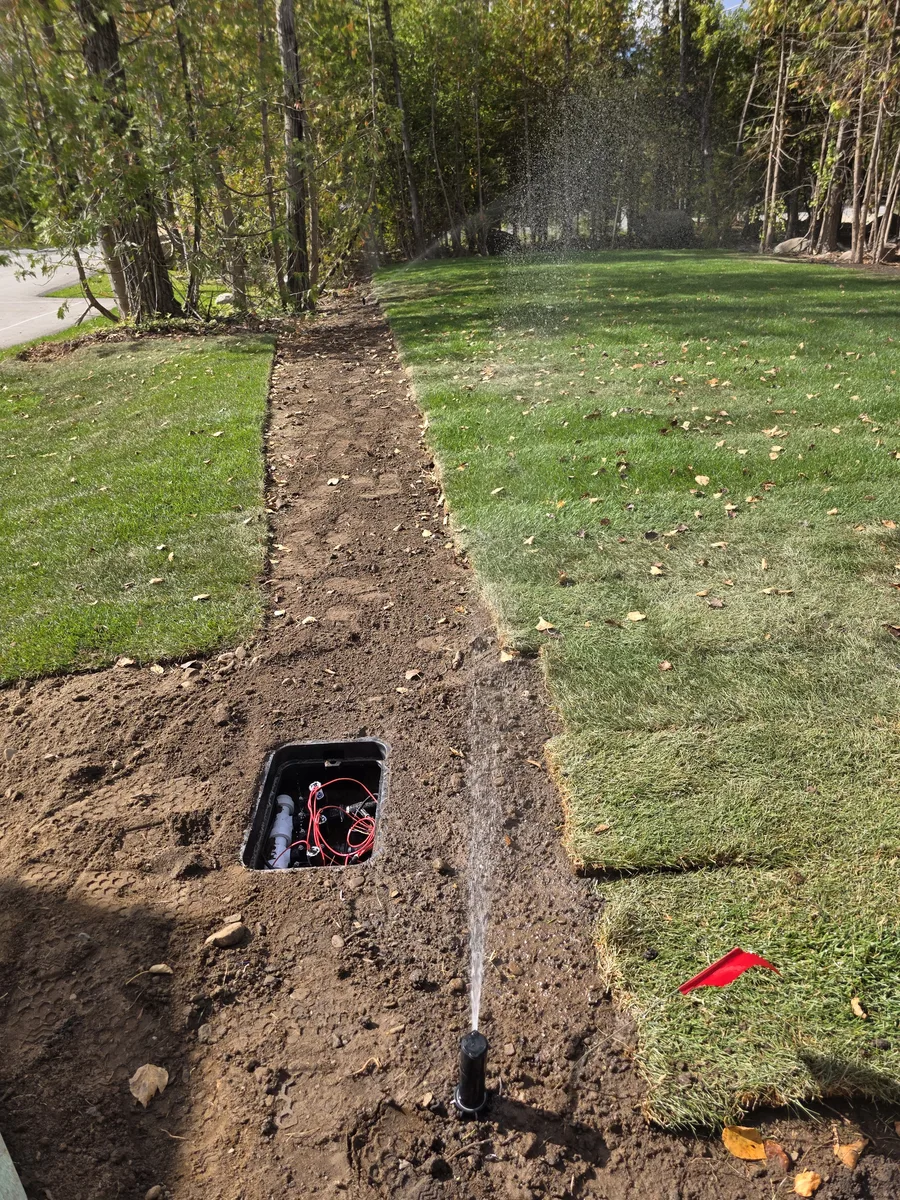 Open irrigation valve box and a sprinkler head running beside freshly laid sod